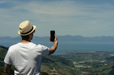 Hawkes Gözcüsü Takaka Tepesi 'nde akıllı telefonuyla selfie çeken genç bir adam. Yeni Zelanda