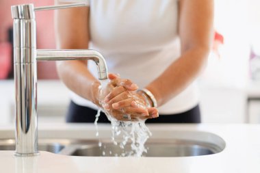 Genç bir kadın ellerini muslukta duruluyor. Önleme ve yeni normal kavram.