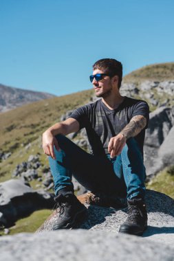 Genç adam bir kayanın üzerinde oturuyor ve Castle Hill, Yeni Zelanda 'daki manzaraya bakıyor. Narnia Film Seti. Normal İnsanlar konsepti