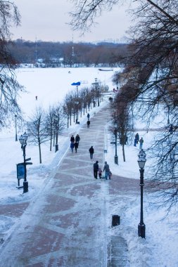 Moskova, Rusya-Aralık, 27, 2020: Tsaritsyno Parkı 'ndaki yaya yolu boyunca yürüyen insanların manzarası soğuk bir kış gününde beyaz kar ve çıplak ağaçların arkasında.