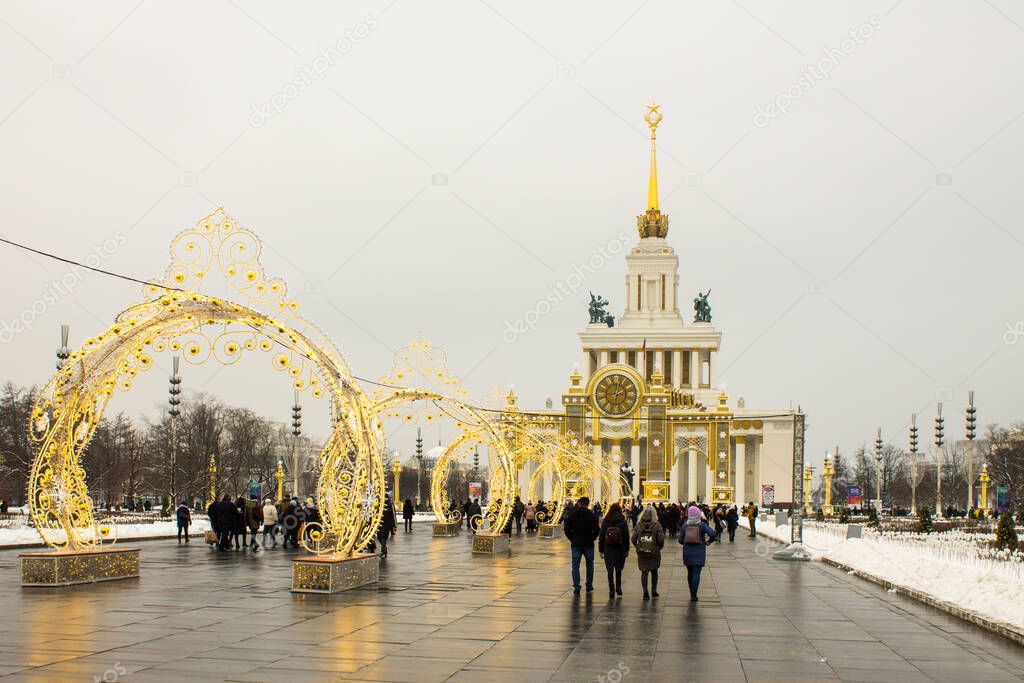 Moscow, Russia-January, 7, 2021: panoramic view of vdnkh Park with historical palaces pavilions and New Year decorations and people walking on a cloudy winter day and space for copying