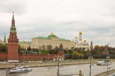 Moskova / Rusya - 5 Mayıs 2021: Tuğla duvar manzarası, sarı Grand Kremlin Sarayı ve Moskva Nehri kıyısında bulutlu bir bahar gününde altın kubbeleri olan Varsayım Katedrali