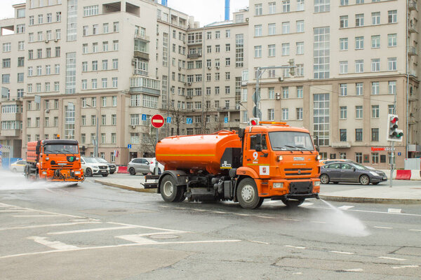 Moscow, Russia-May, 5, 2021: orange bright official car water carrier drives down the street of the city and washes the asphalt spraying water jets on the road against a gray building