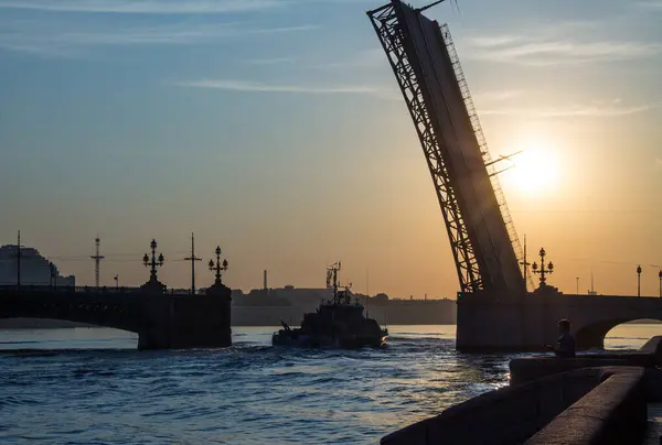 オープン トリニティ橋の暗いシルエットと美しい黄金の夜明けとサンクトペテルブルクの朝日を背景にそれを通過する軍艦ロシア — ストック写真
