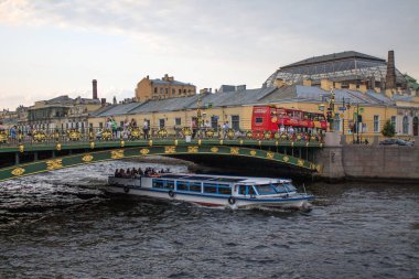 Şehrin tarihi merkezinde, Saint-Petersburg Rusya 'da gün batımında güzel mimarisi olan su kanalı boyunca güzel bir köprünün altında turistik bir feribot yelken açar.