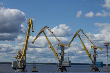 VYBORG, Leningrad REGION, RUSSIA-JULY, 19, 2021: Bulutlu bir yaz gününde körfezin kıyısında yüklenen sarı iskele vinçleri