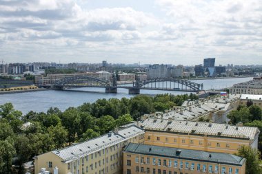 Saint Petersburg, Rusya, 20 Temmuz 2021: Smolny 'nin çan kulesinden güneşli bir yaz gününde Bolsheokhtinsky metal köprüsü ve evlerin çatıları ile Neva Nehri' nin panoramik üst manzarası