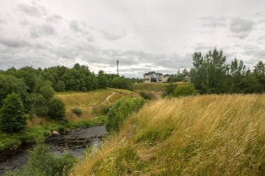 Güzel bir manzara - Tosna Nehri bulutlu bir yaz gününde yeşil tepeler arasında akar ve Rusya 'nın Leningrad bölgesinde en tepede bir kulübe