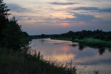 Güzel, mor bir gün batımı ve Moskova sahillerinde ağaçların siluetleriyle Klyazma Nehri 'nde bulutlu, dramatik bir gökyüzünün yansıması.