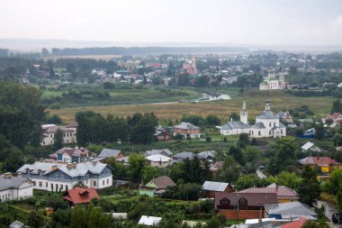 Bulutlu bir yaz gününde evlerin çatıları ve ağaçların yeşil yapraklarıyla tarihi Suzdal kasabasının panoramik manzarası.