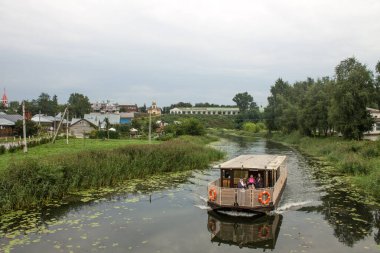 Suzdal Rusya 'da bulutlu bir yaz gününde, yemyeşil bitki örtüsüyle eski kasabadaki küçük Kamenka nehri boyunca yelken açar.
