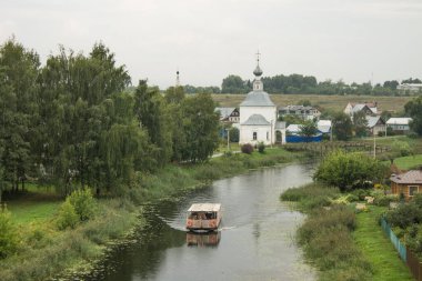 Suzdal Rusya 'da bulutlu bir yaz gününde, yemyeşil bitki örtüsüyle eski kasabadaki küçük Kamenka nehri boyunca yelken açar.