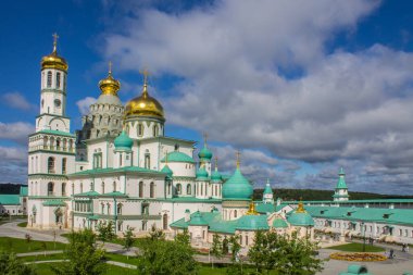 Güneşli bir yaz gününde Yeni Kudüs 'te altın kubbeli beyaz taş kiliselerin ünlü mimari topluluğu Istra Moskova bölgesinde dramatik bulutlarla dolu açık mavi bir gökyüzüne karşı.