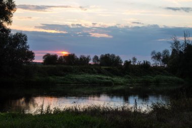 Güzel dramatik gün doğumu - güneş bulutlu bir gökyüzü ve kıyıdaki karanlık ağaç siluetleri üzerinde yükseliyor