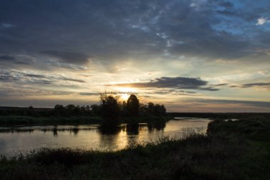 Nehrin üzerinde güzel bir gün doğumu ve ağaçların siyah siluetleri yaz sabahının erken saatlerinde bulutlu ve dramatik bir gökyüzünün arka planına karşı kopyalanacak bir yer.