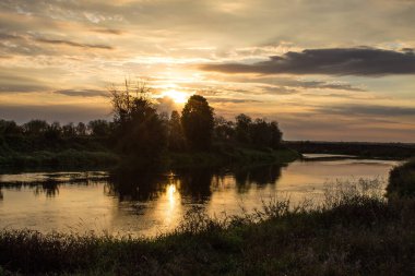 Nehrin üzerinde güzel bir gün doğumu ve ağaçların siyah siluetleri yaz sabahının erken saatlerinde bulutlu ve dramatik bir gökyüzünün arka planına karşı kopyalanacak bir yer.