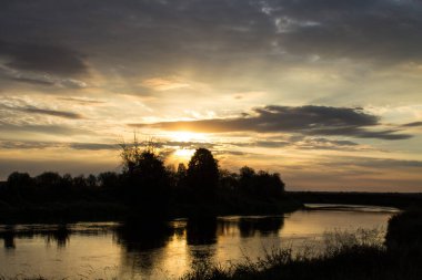 Nehrin üzerinde güzel bir gün doğumu ve ağaçların siyah siluetleri yaz sabahının erken saatlerinde bulutlu ve dramatik bir gökyüzünün arka planına karşı kopyalanacak bir yer.