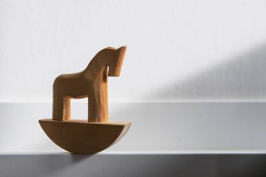 Küçük ahşap sallanan at oyuncağını beyaz güneşli duvar arkasına yakın tut.