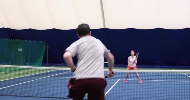 Uomo e donna giocano a tennis su un campo coperto — Video Stock