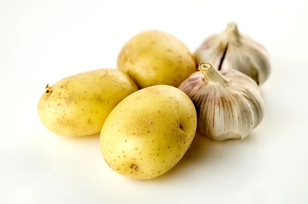 Patatas sin pelar y cabezas de ajo altas en carbohidratos aisladas en blanco —  Fotos de Stock