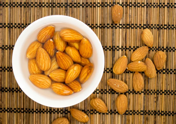 Soaked almonds in a bowl against a straw mat — Stock Photo, Image