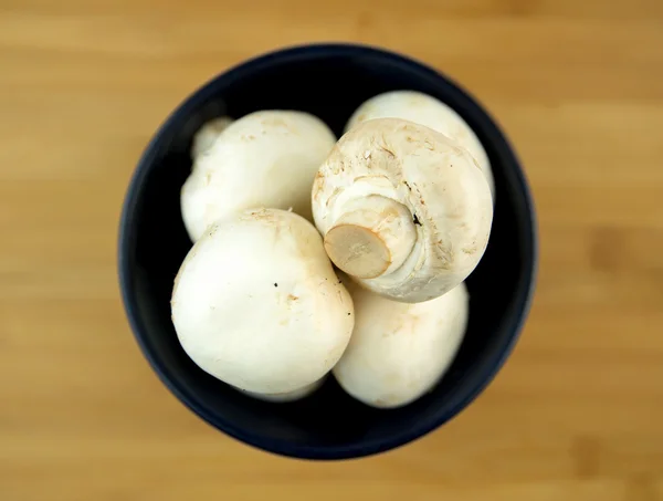 Белые грибы в черной чаше на деревянной доске — стоковое фото