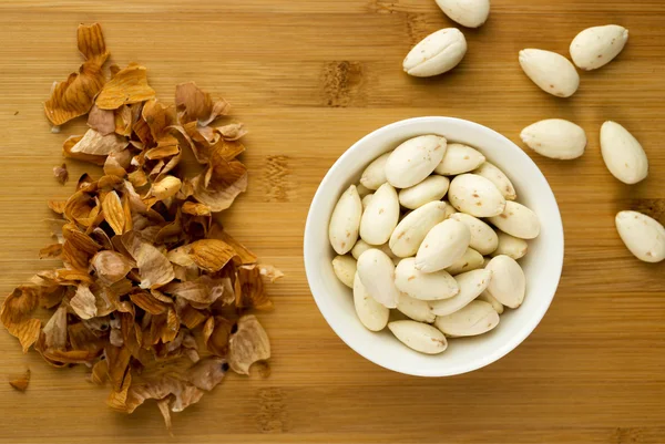 Blanched almonds in a bowl next to almond peels — Stock Photo, Image