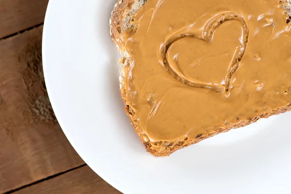 Peanut butter toast with heart shape on white against wooden boa — Stock Photo, Image