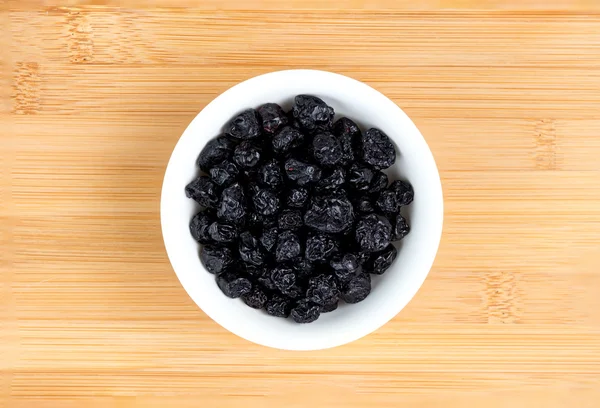 Dehydrated blueberries in bowl against wooden board — Stock Photo, Image