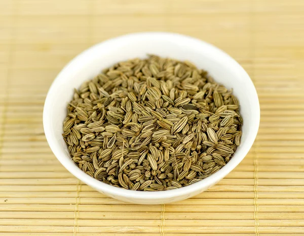 Cumin seeds in bowl against wooden background — Stock Photo, Image