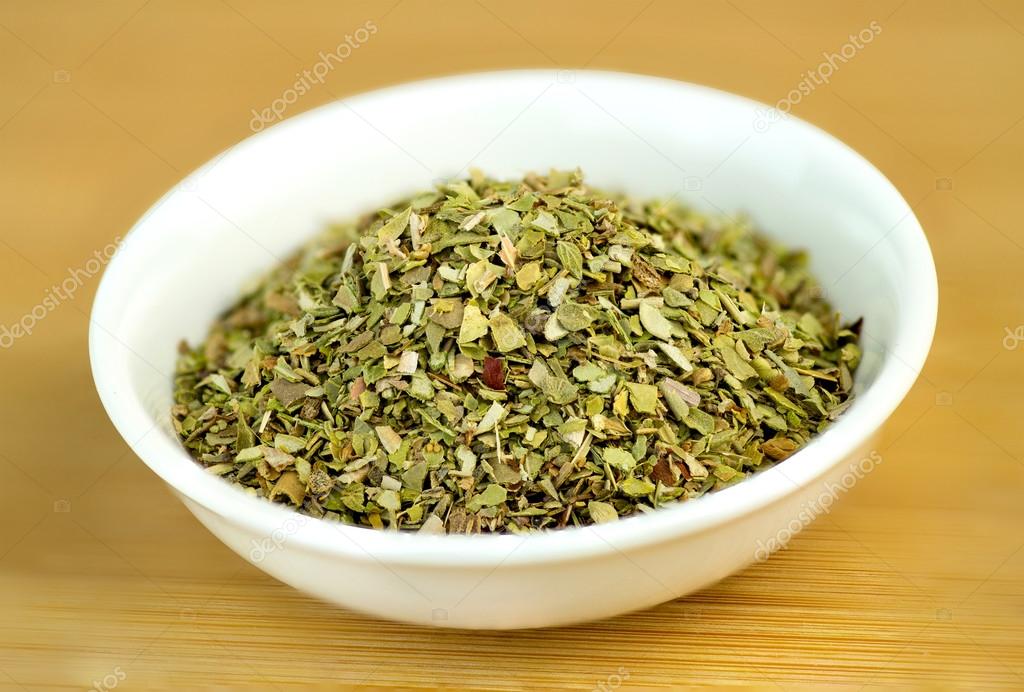 Dehydrated oregano macro in white bowl on wooden background