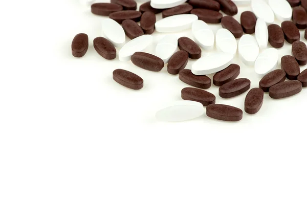 Comprimidos comprimidos marrones y blancos dispersos en el fondo blanco aislado — Foto de Stock