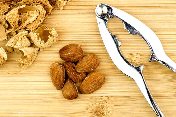 Almendras, conchas con cascanueces de metal sobre fondo de madera —  Fotos de Stock