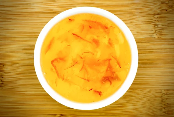 Engarrafamento de marmelada de laranja em um boliche branco contra uma mesa de madeira — Fotografia de Stock