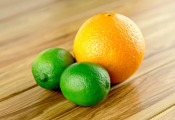 Duas limas e uma laranja contra fundo rústico — Fotografia de Stock