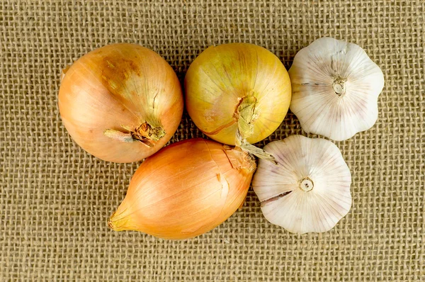 Overhead macro of garlic and onion root veggies on hessian mater — Stock Photo, Image