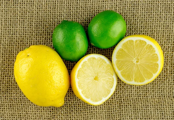 Bütün ve kesme parlak sarı limon ve parlak yeşil limes burl üzerinde — Stok fotoğraf