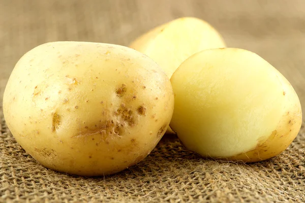 Macro of whole unpeeled potatoe next to cut pieces — Stock Photo, Image