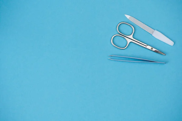 Nail scissors, tweezers and nail file lying on blue background with copy space — Stock Photo, Image
