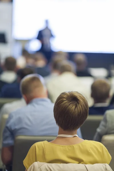 People at the Business Conference Listening to the Speaker Standing in Front of a Big Board on Stage