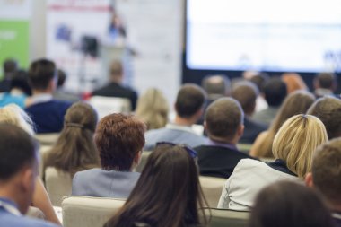 Büyük seyirci önünde iş toplantısında konuşan kadın ev sahibi.