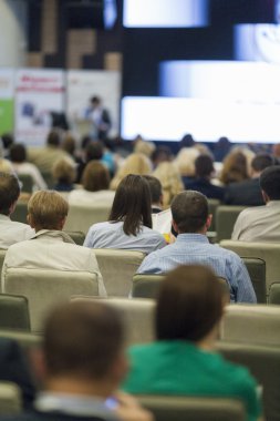 Büyük seyirci önünde iş toplantısında konuşan kadın ev sahibi