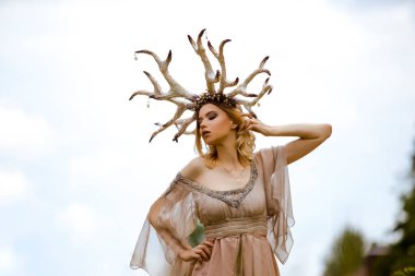 Süslü Geyik Boynuzları ile açık havada Parlak Gökler 'e Karşı Hafif Elbiseli, Şehvetli Genç Kafkas Kız Pozu. Yatay Resim Yönlendirmesi