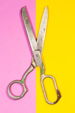 Pembe ve sarı kâğıt üzerine yerleştirilmiş eski paslı terzi makası. Dikey resim