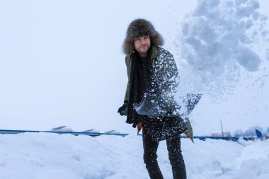 Kışın giyinmiş yakışıklı bir adamın portresi. Şehir ortamında karları kürekle fırlatıp atıyor. Yatay resim