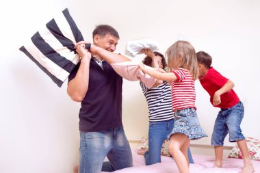 Aile Birliği Fikirleri. Mutlu Kafkasyalı Dört Kişilik Aile Evde Olumlu Duygularla Yatakta Eğlenceli Bir Yastık Dövüşü Yapıyor. Yatay Resim Kompozisyonu