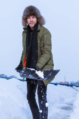 Kışın giyinmiş yakışıklı bir adamın portresi. Şehir ortamında karları kürekle fırlatıp atıyor. Dikey Yönlendirme