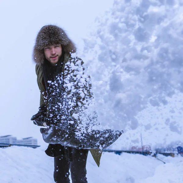 Kışlık kıyafetli, İşkolik Kafkasyalı Yakışıklı Adam 'ın Şehir Ortamına Kürekle Kar Fırlatan portresi. Kare Resim Kompozisyonu