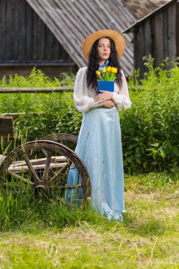 Kırsal yaşam tarzı. Açık havada kitap okurken, eski moda çiçeklerle süslenmiş, esmer, sakin bir kız pozu. Dikey Resim Yönlendirmesi