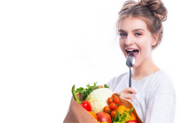 Sağlıklı beslenme. Beyaz arka plana karşı kaşıkla poz veren birden fazla sebze ve market malzemesiyle dolu Eko Kağıt Torbalı Mutlu Beyaz Kız. Yatay Resim Yönlendirmesi